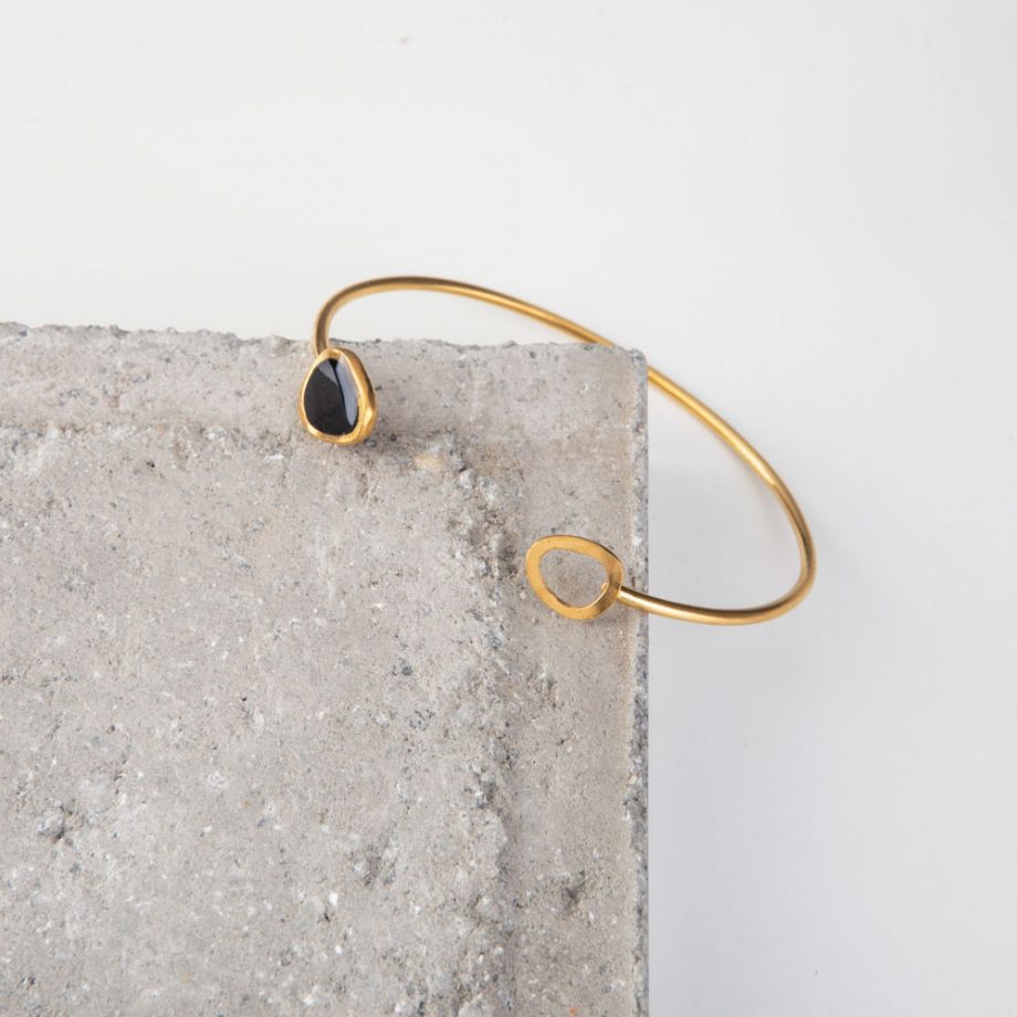 An elegant and unique adjustable gold-plated bangle with oval loops at either end. This contemporary cuff bracelet has been hand crafted in 24K gold-plated brass, with a high shine finish. The two oval loops soldered at each end are approximately 1cm long by 2.5mm wide and give a touch of sophistication to this minimalist cuff.