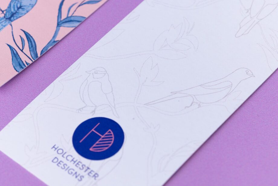 Close up of the monochrome side of the Brighton Birds bookmark with a white background and light grey line-drawing version of the illustration. Next to is is an out of focus corner of the bookmark's other side.