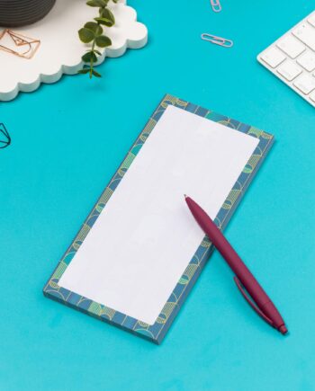 Deco delights list pad - teal gradient background with golden yellow deco motif - is on a teal desk with pen, white keyboard and paperclips surrounding it.