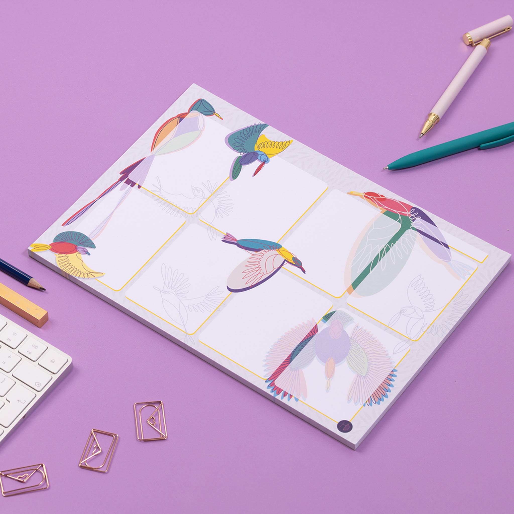 A4 Planner pad with a light grey background and various multi-coloured line drawn bird illustrations around it. there are 8 white boxes, with a top row for a date, and the birds are mainly behind these, although some overlap at the edges. The pad is on a deep lilac desk with a white keyboard and pens surrounding it.