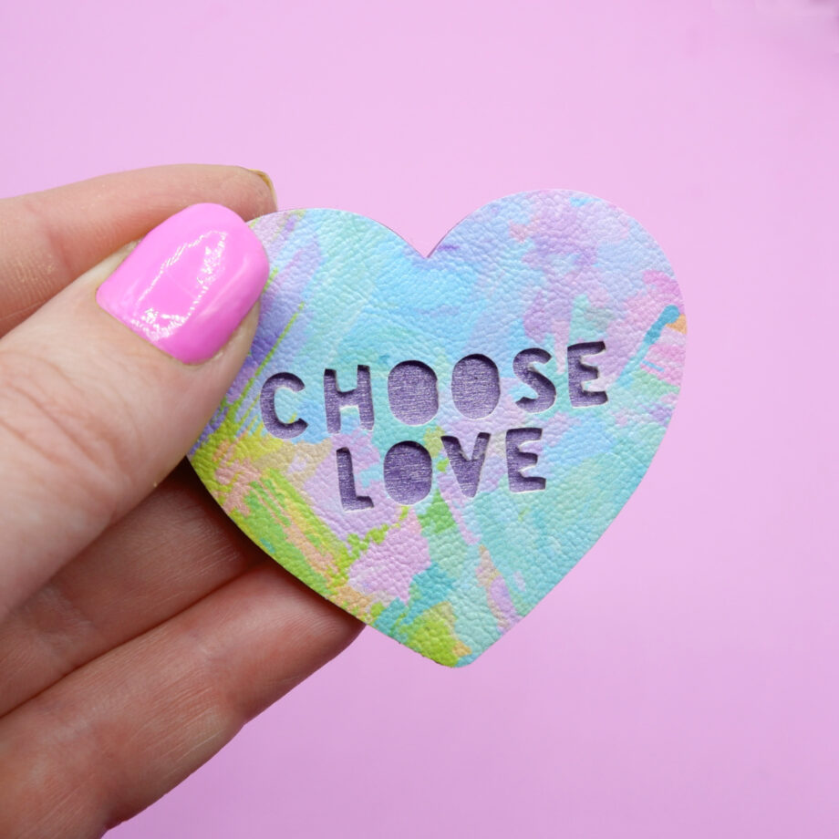 Rainbow coloured, Choose Love heart-shaped brooch, held in hand