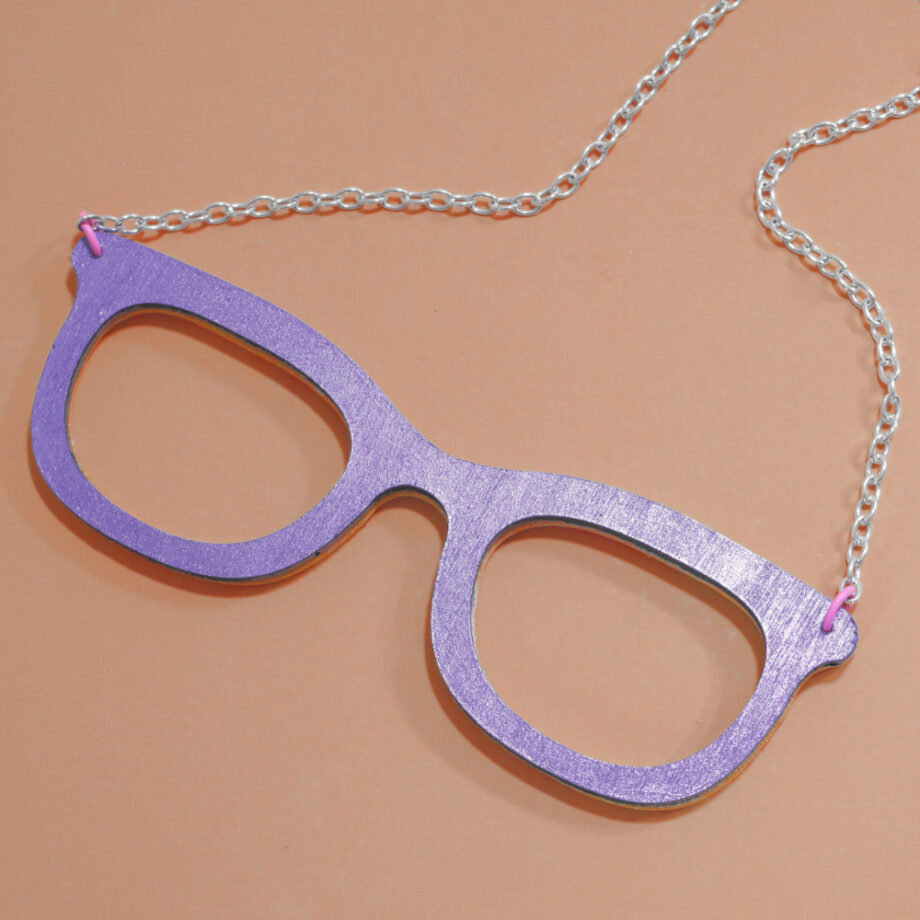 Showing the reverse side: Metallic purple painted wood backing of a glasses-shaped necklace.