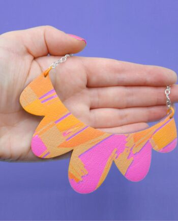Handmade faux leather necklace and wood with a scalloped edge and a hot pink, orange, and purple abstract design.