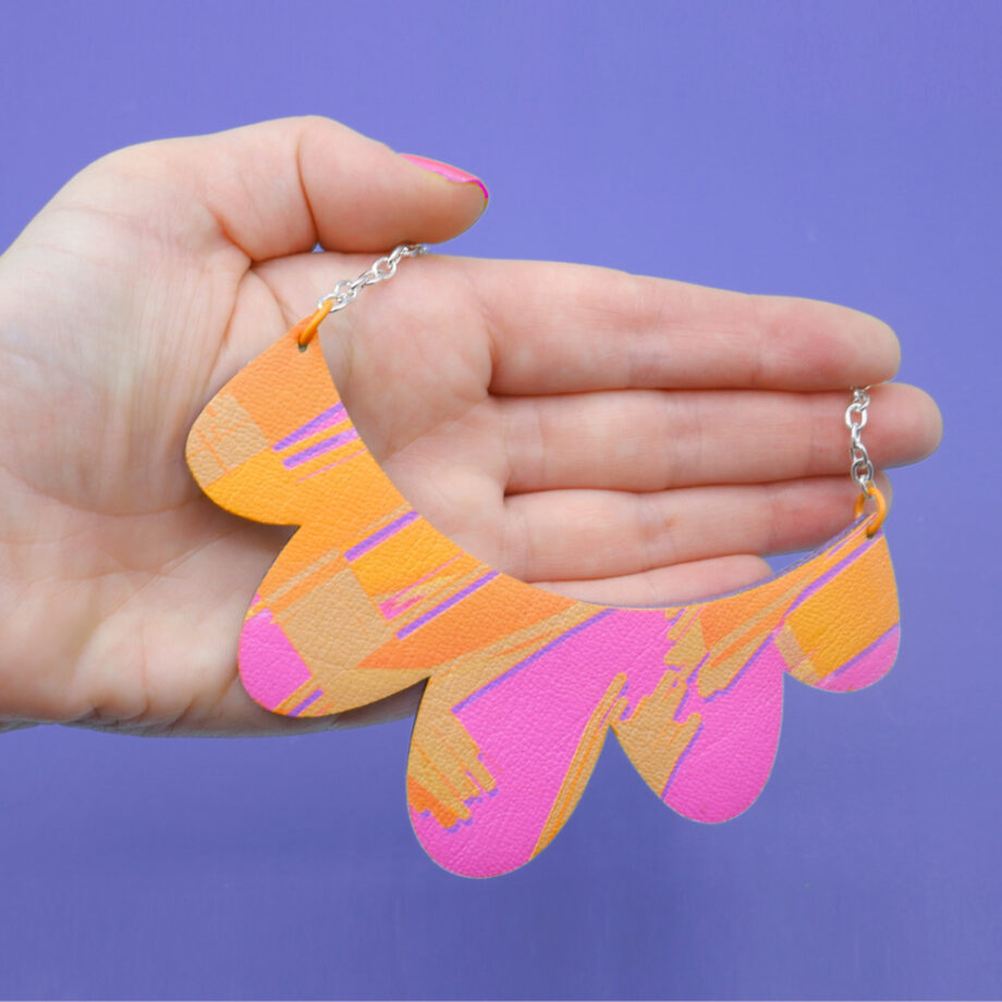 Handmade faux leather necklace and wood with a scalloped edge and a hot pink, orange, and purple abstract design.