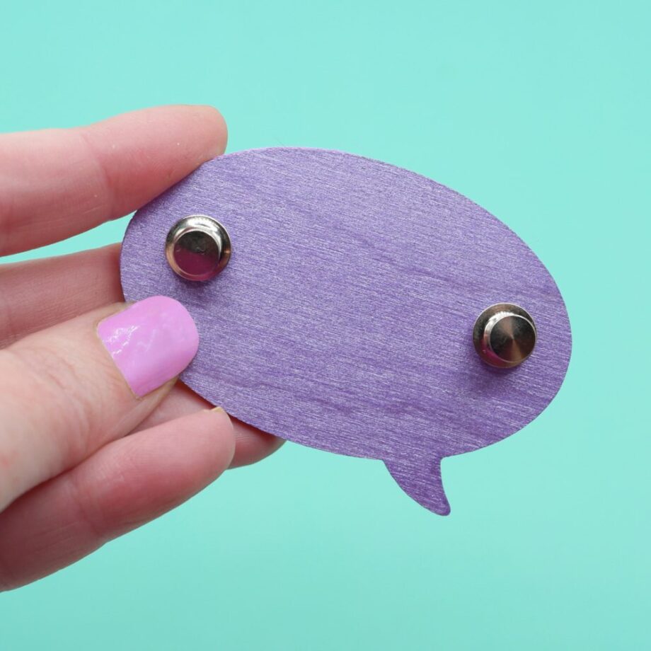 The reverse side of a handmade speech bubble brooch, showing off the metallic purple paint colour and locking pins