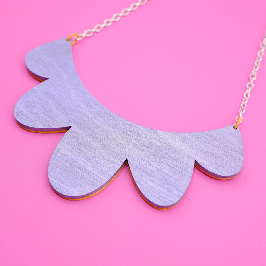 Reverse of a handmade necklace, seen is the metallic purple painted birch plywood complete with genuine silver plate chain against a hot pink background.