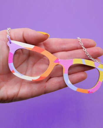 Unique, handmade glasses pendant necklace with a vibrant, geometric abstract design on faux leather.