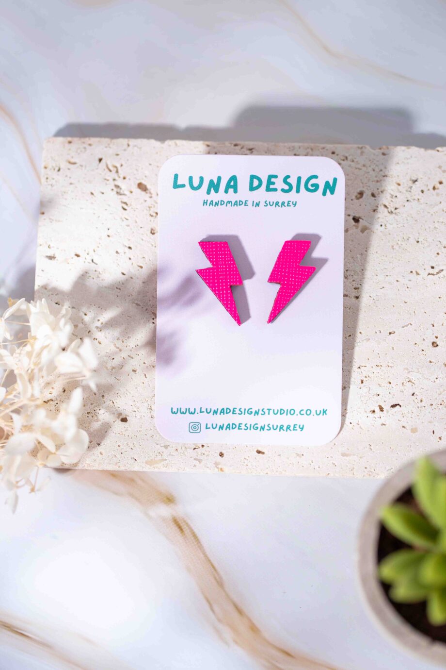 A pair of handmade lightning bolt studs in neon pink Displayed on a Luna Design card.