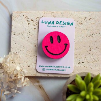 Neon Pink Smiley Brooch displayed on a Luna Design branded card against a neutral stone background.