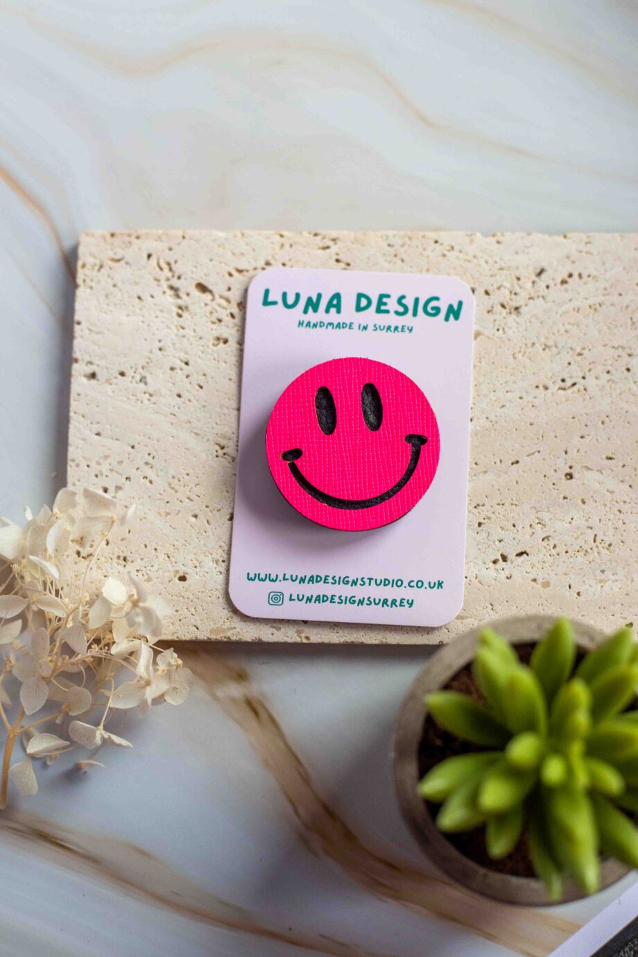 Neon Pink Smiley Brooch displayed on a Luna Design branded card against a neutral stone background.