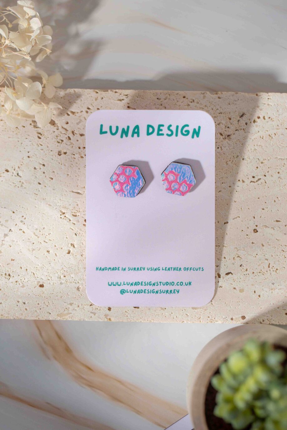 Pair of leather hexagon stud earrings in an iridescent white colour with pink sequin waste pattern