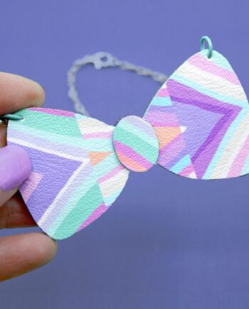 Pastel bow shaped necklaced handmade with modern striped faux leather fabric attached to a wooden base