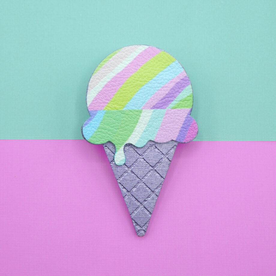 Pastel ice cream brooch with a drippy scoop design in soft lilac, mint, and pink stripes, paired with a textured metallic purple cone. A playful and colourful accessory, photographed against a split mint green and pink background.