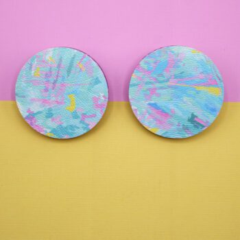 Pair or abstract patterned pastel blue, pink and yellow, circular stud earrings on a split coloured card of pink and yellow