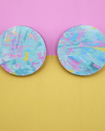 Pair or abstract patterned pastel blue, pink and yellow, circular stud earrings on a split coloured card of pink and yellow