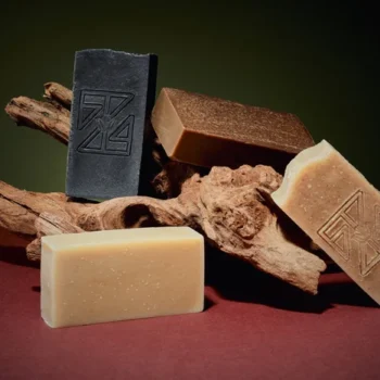 Handcrafted turmeric and camwood cold process soap bar with a rich golden-brown color, made with shea butter and olive oil, displayed on a natural-toned wooden stick.