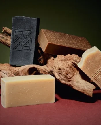 Handcrafted turmeric and camwood cold process soap bar with a rich golden-brown color, made with shea butter and olive oil, displayed on a natural-toned wooden stick.