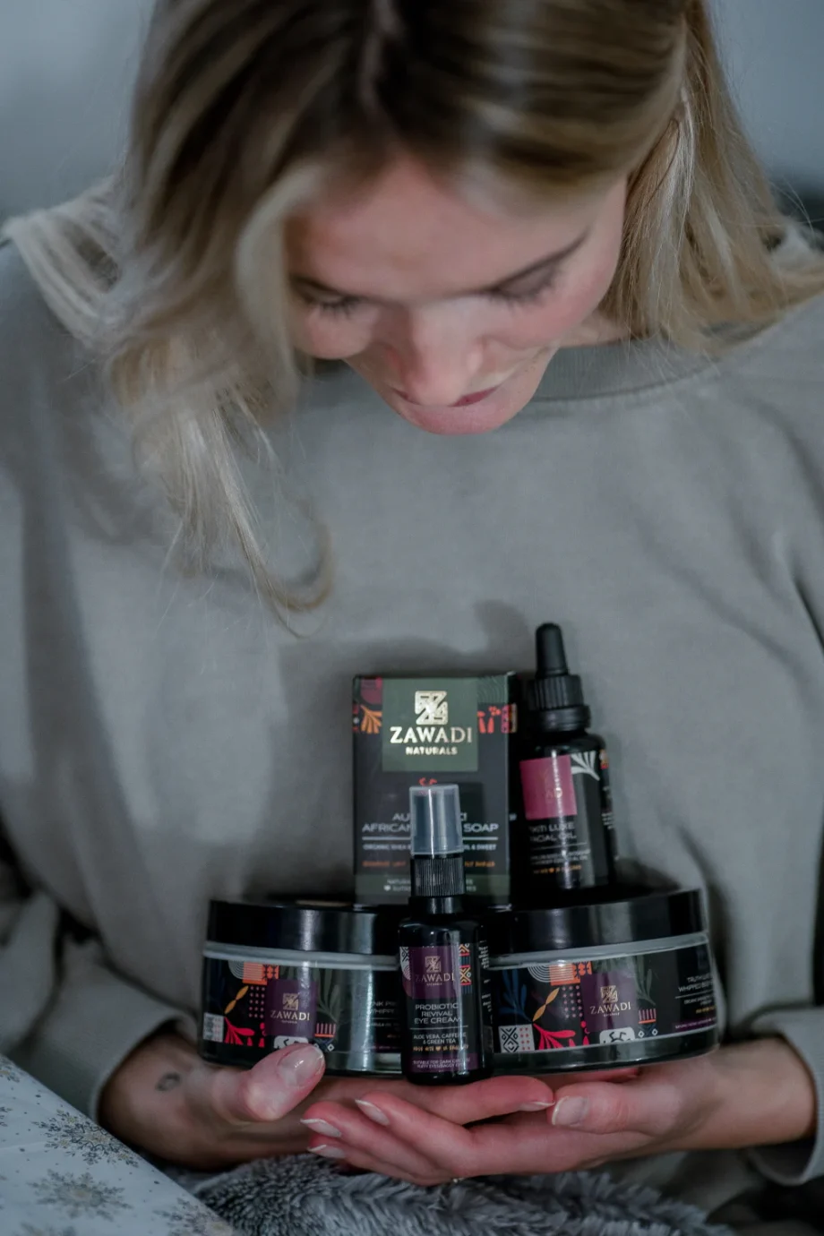 Smiling woman holding authentic African black soap and Zawadi Naturals skincare products, celebrating natural beauty and wellness