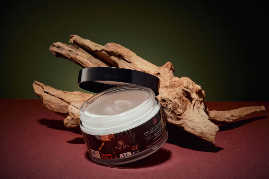 Jar of Pink Prestige whipped natural shea butter on display next to wood, showcasing its smooth, white color