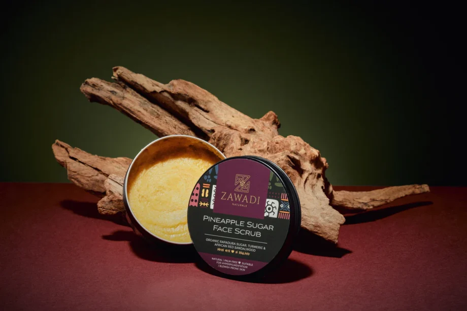 Open jar of Pineapple, Camwood & Turmeric Sugar Scrub on a wooden stick, showing rich texture and golden hue