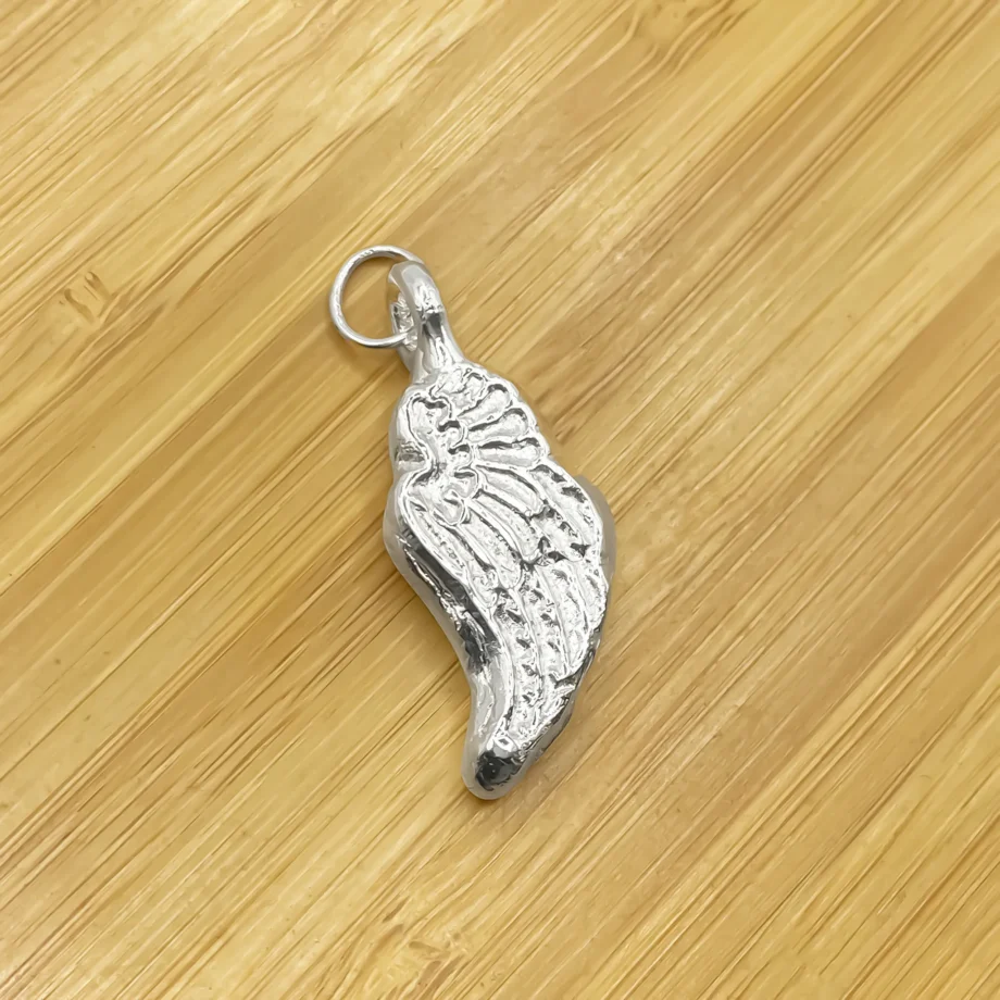 Close-up of silver angel wing pendant on wood background