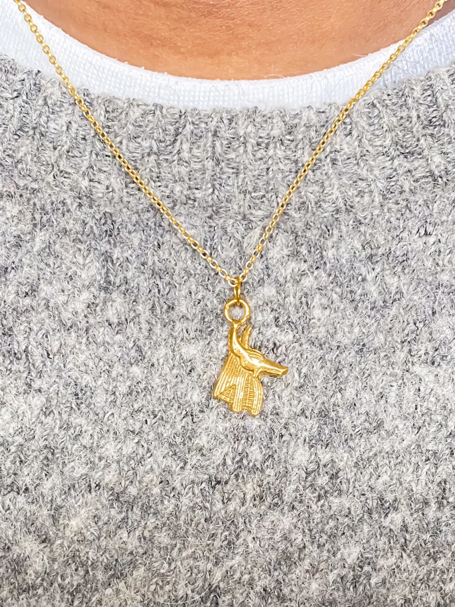 Gold Anubis pendant worn over a grey sweater