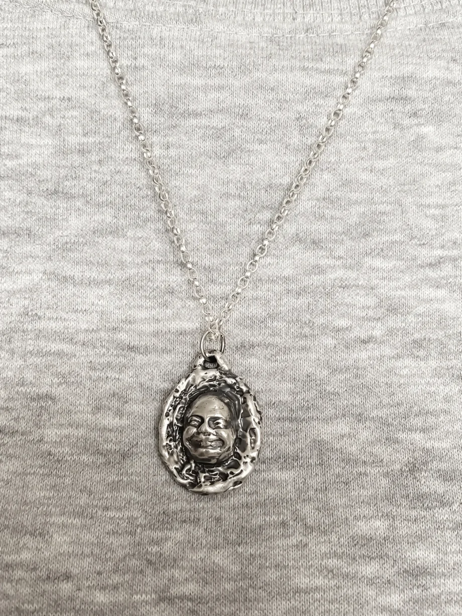 Buddha Face Pendant worn on chest over grey top, close-up