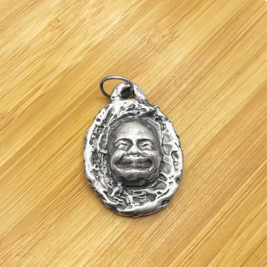 Buddha Face Pendant resting on wooden surface, handcrafted in sterling silver