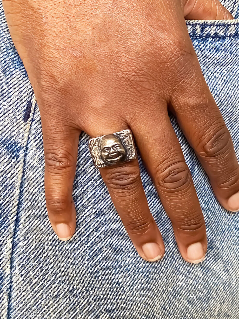 Buddha Face Ring worn on middle finger against denim background