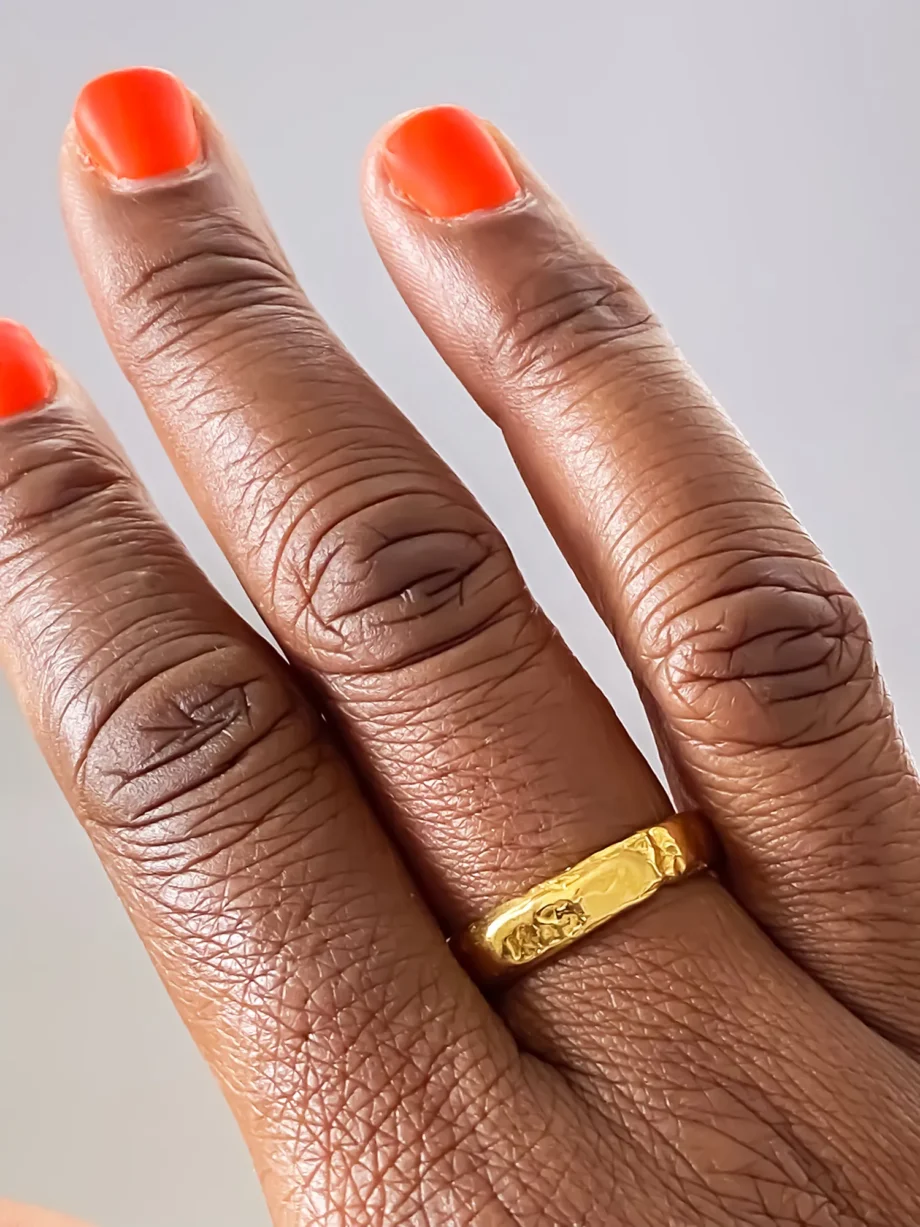 Two gold textured rings worn on hand with orange nail polish