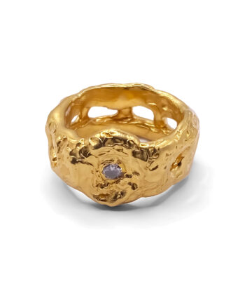 Sculptural gold ring with white gemstone on plain background