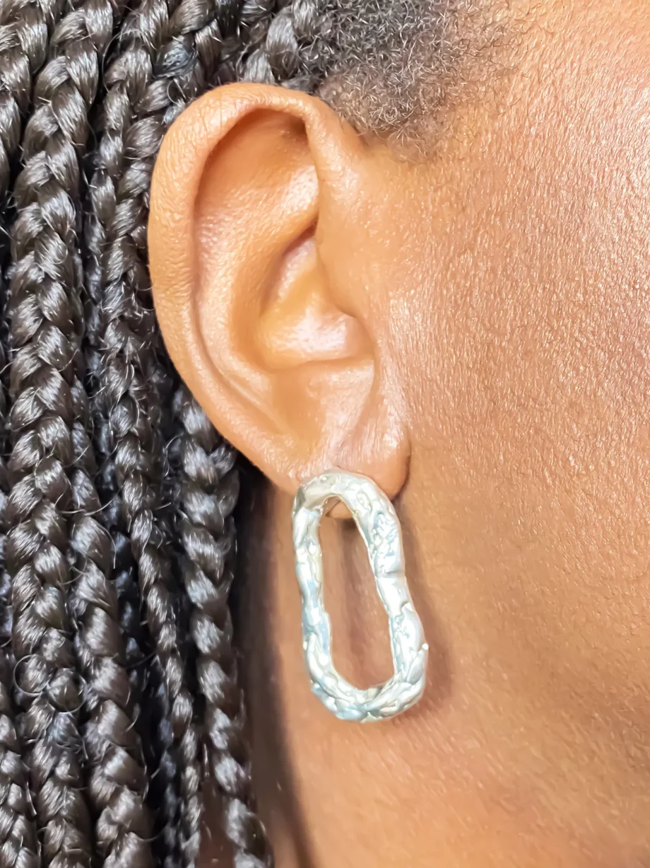 Close-up of silver Flow Loop Earrings worn on ear, showing textured, sculptural design