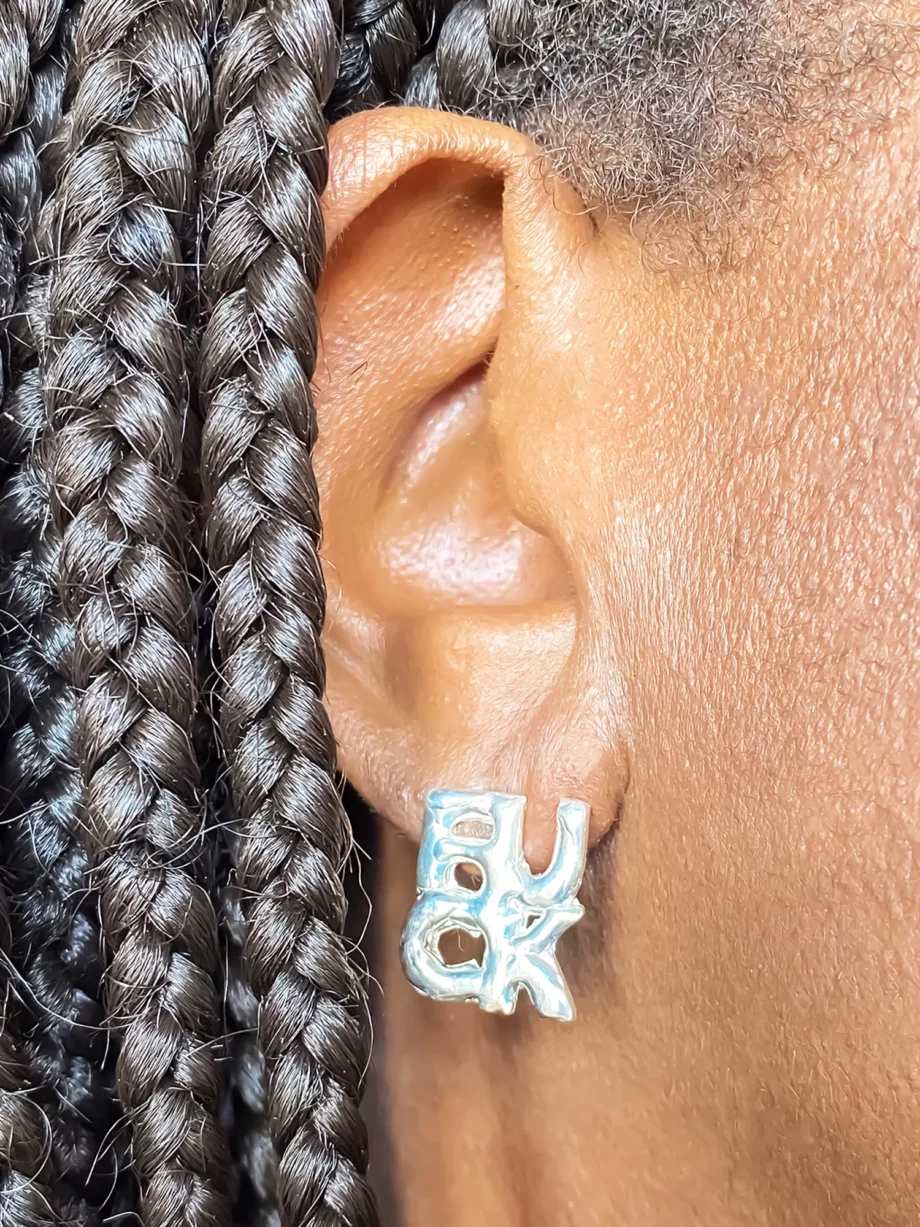 Close-up of silver ‘FUCK’ earring worn on right ear