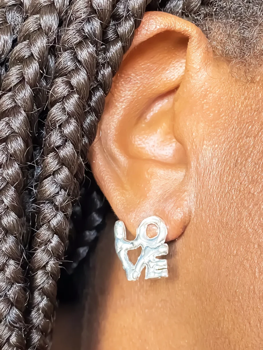 Close-up of silver ‘LOVE’ earring worn on left ear