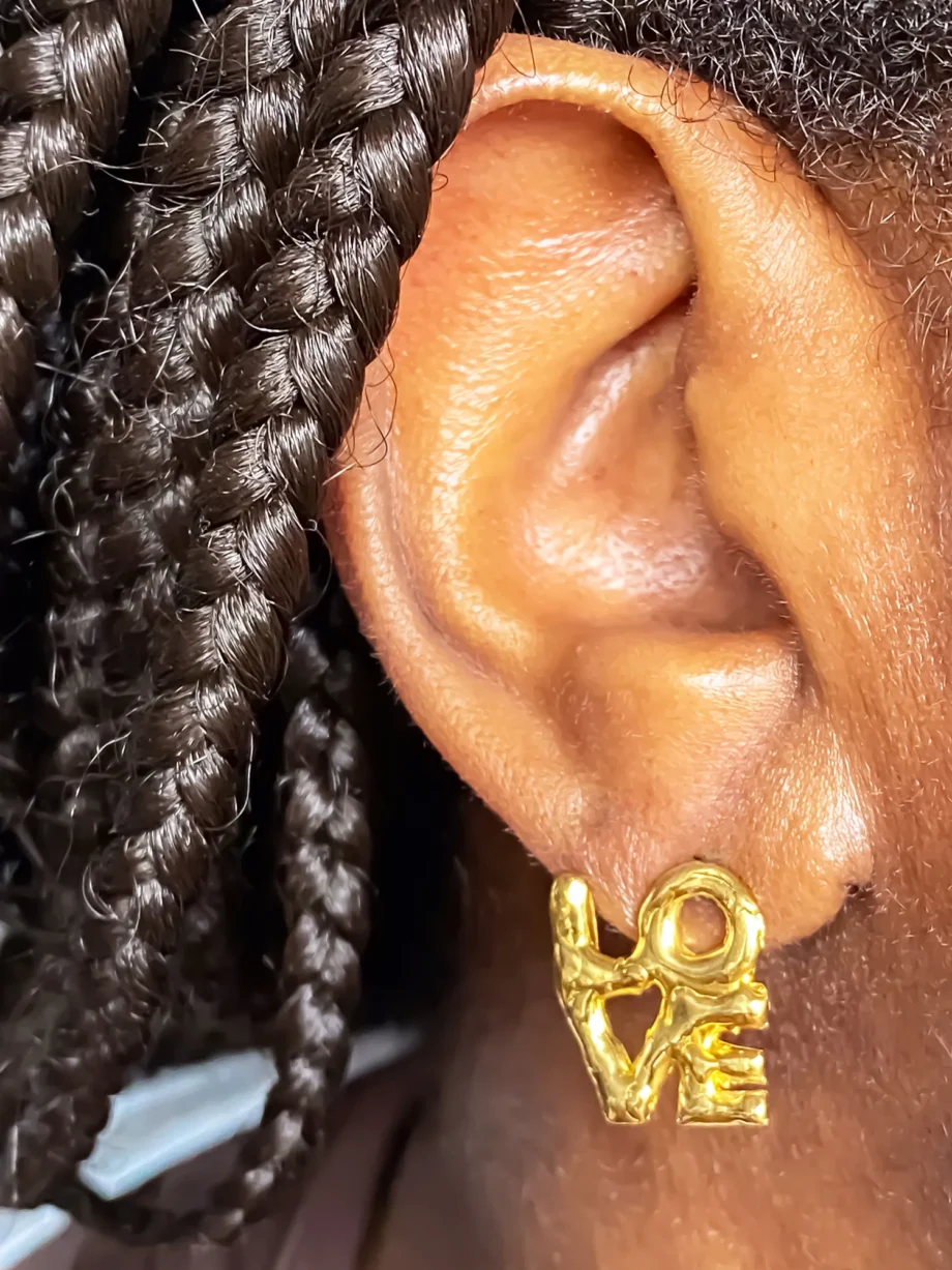 Close-up of gold ‘LOVE’ earring worn on left ear