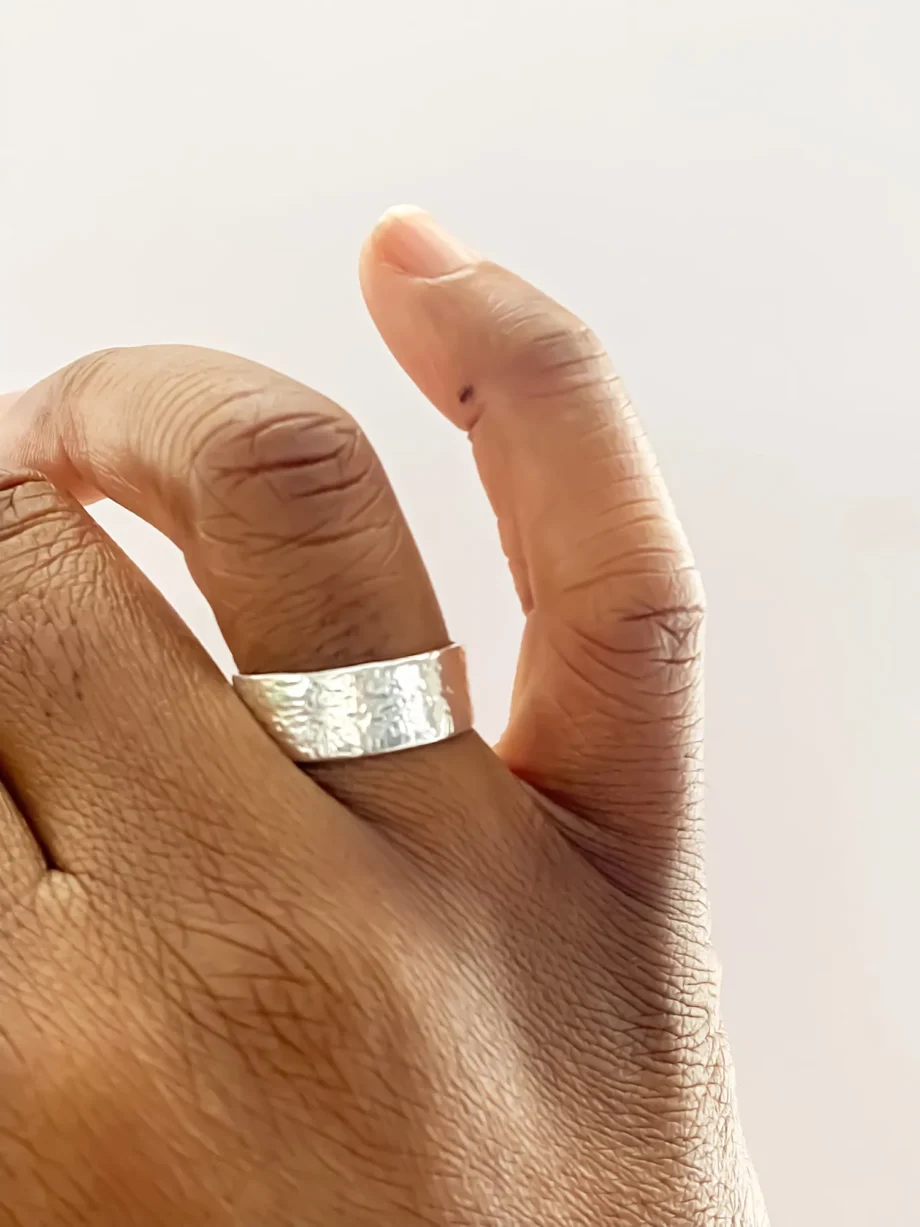 Hammered silver ring worn on a hand, fingers mid-gesture.