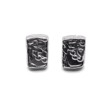 Detailed close-up of rectangular sculpted silver earrings with organic texture