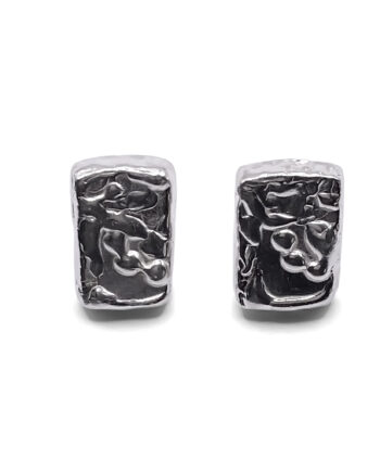 Detailed close-up of rectangular sculpted silver earrings with organic texture