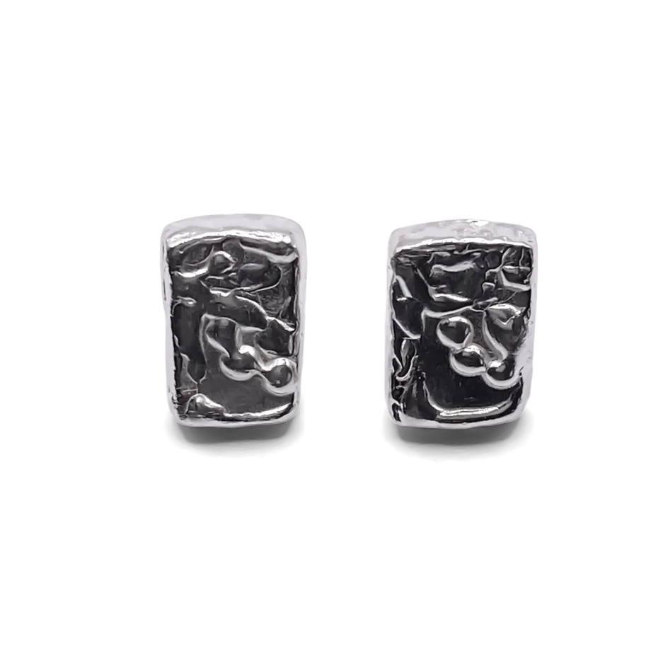 Detailed close-up of rectangular sculpted silver earrings with organic texture