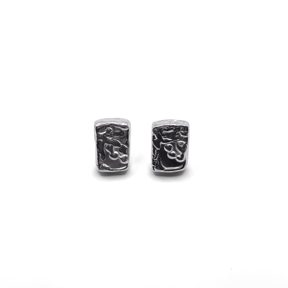 A close-up shot showing the rectangular sculpted earrings worn on the ear. The textured finish catches the light, showcasing the unique detailing and elegant silhouette of each handcrafted piece.
