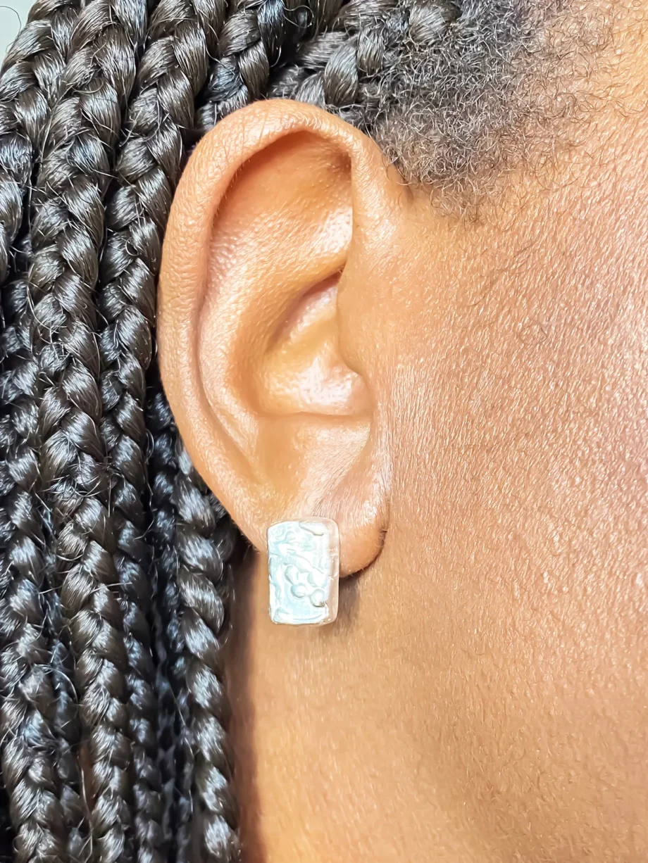 Close-up of a model wearing rectangular sculpted silver earrings with a textured surface