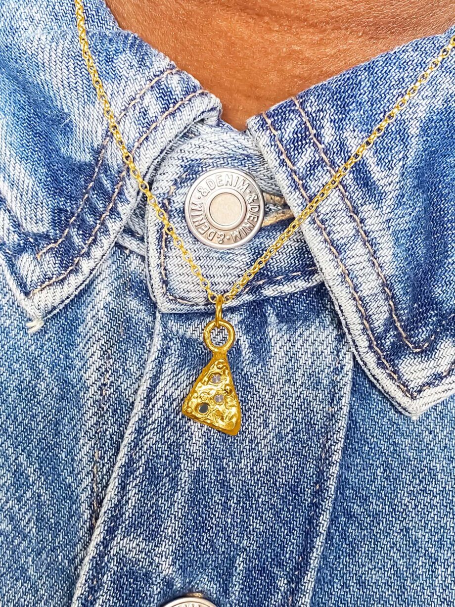 Gold triangular pendant worn over a denim jacket.