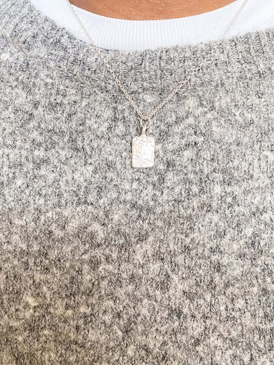 Rectangular sculpted silver pendant necklace worn with grey wool jumper