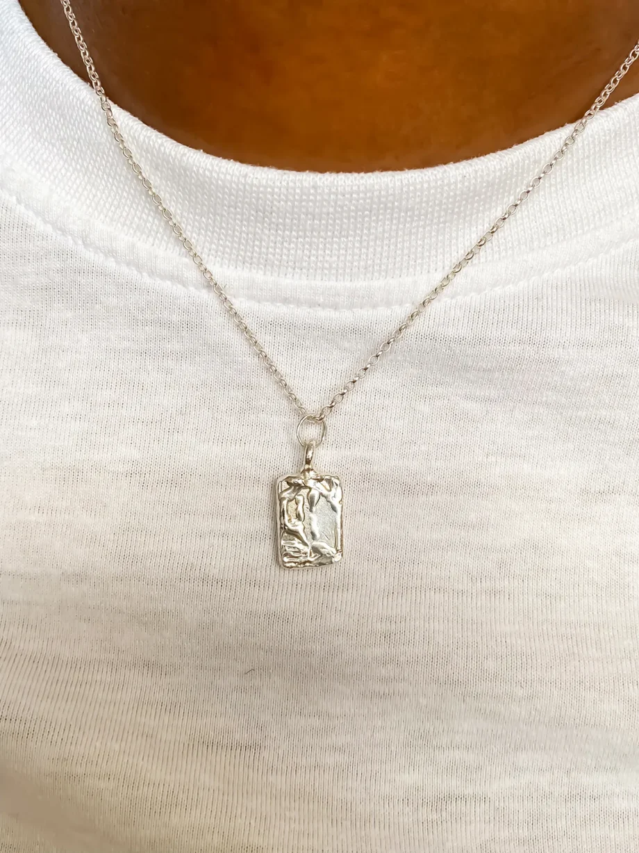 Close-up textured rectangular silver pendant necklace on cream fabric