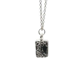 Silver chain necklace with rectangular sculpted pendant flat lay photography