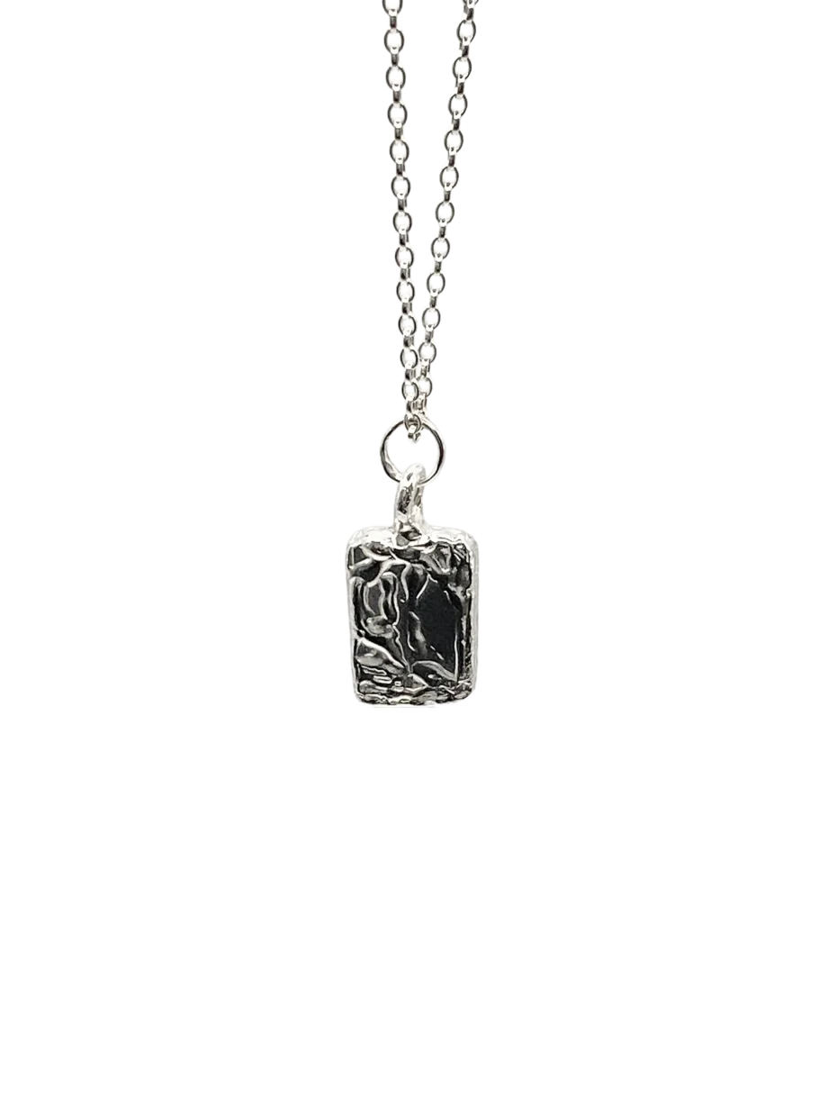 Silver chain necklace with rectangular sculpted pendant flat lay photography