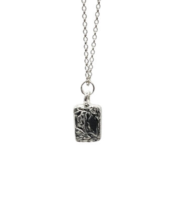 Silver chain necklace with rectangular sculpted pendant flat lay photography