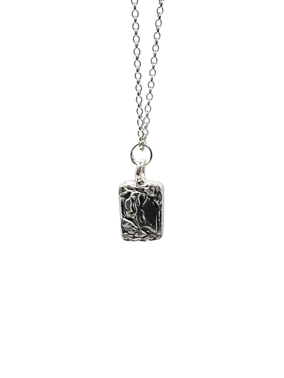 Silver chain necklace with rectangular sculpted pendant flat lay photography