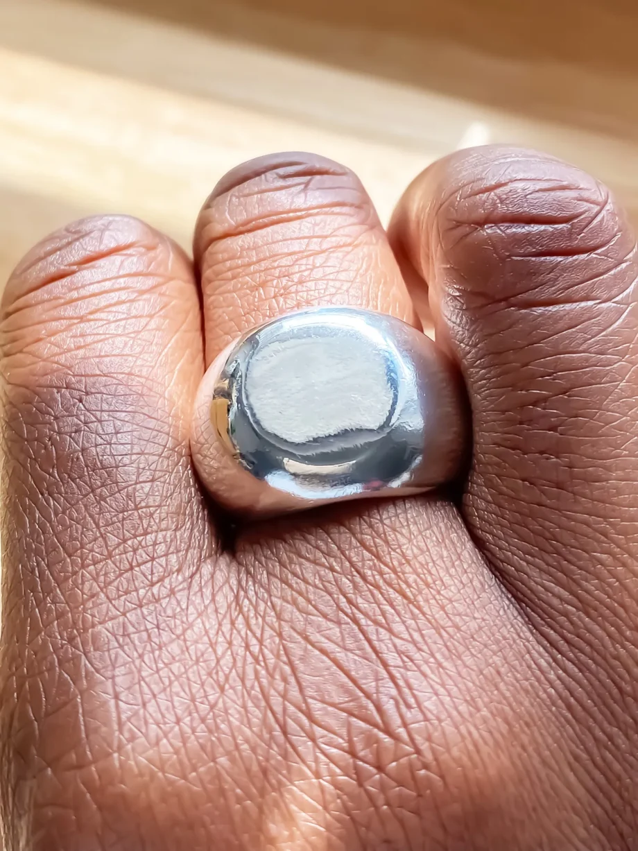 Close-up of a round silver signet ring on a hand, reflecting ambient light.