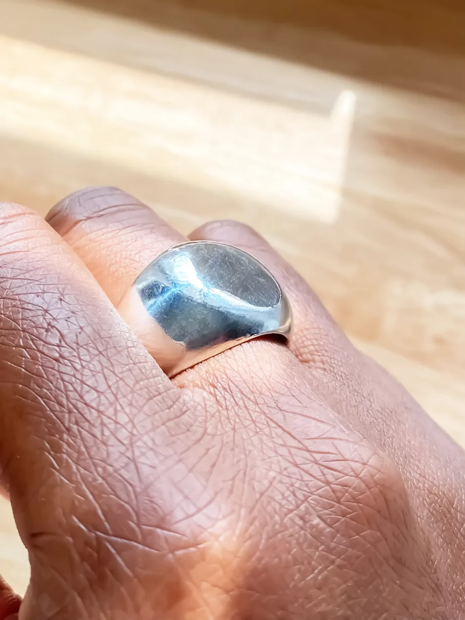 Polished round silver signet ring worn on a hand, reflecting natural light.
